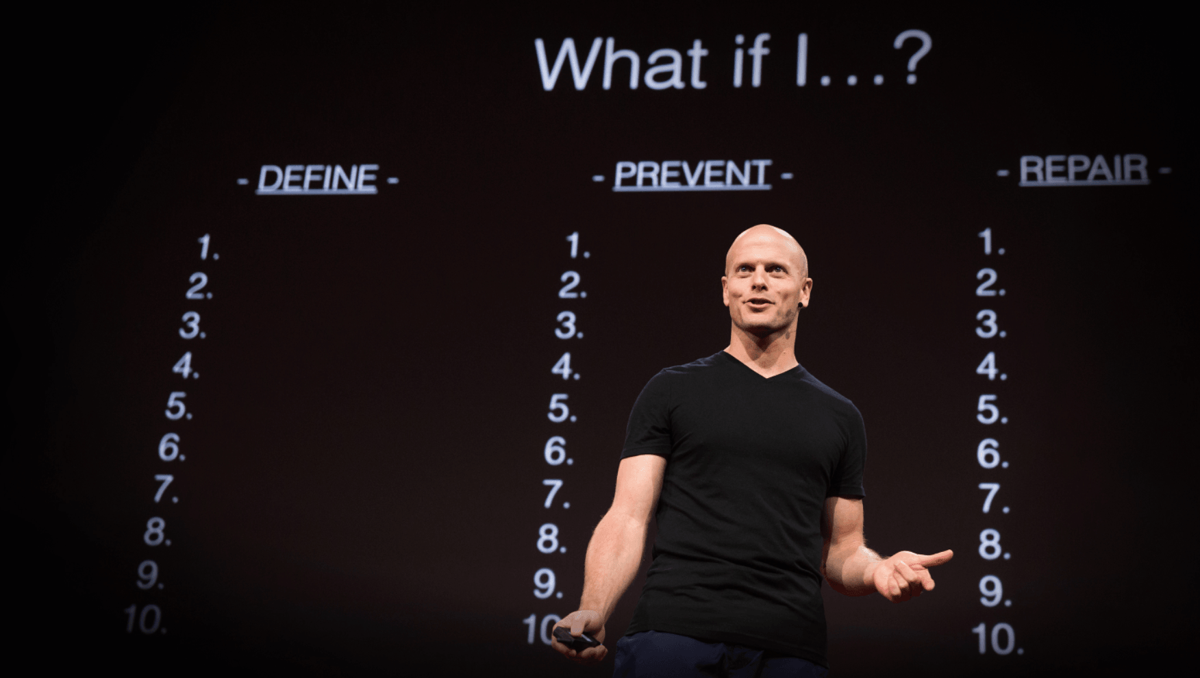 Tim Ferriss standing on stage speaking with what if on the screen behind